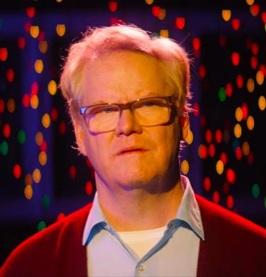 Man looking a little confused, standing  in front of twinkling lights